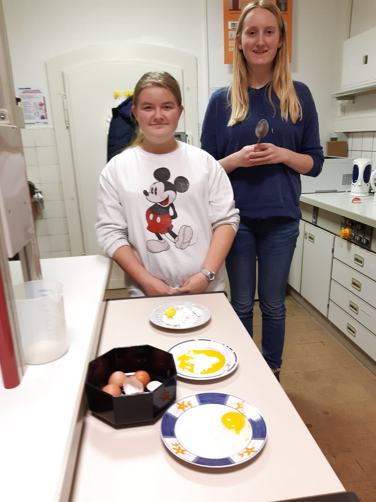 Zwei Schülerinnen stehen vor drei Tellern mit Spiegeleiern